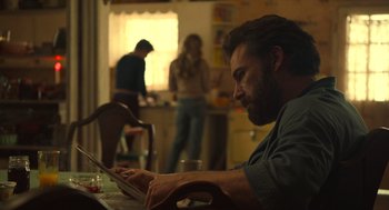 Movie still from “The Tender Bar” (2021), directed by George Clooney – A man sitting at a table using a laptop; Medium shot, Over the shoulder angle