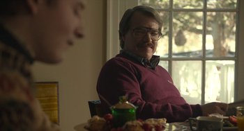 Movie still from “The Tender Bar” (2021), directed by George Clooney – A man sitting at a table in front of a plate of food; Medium shot, Over the shoulder angle