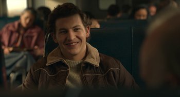 Movie still from “The Tender Bar” (2021), directed by George Clooney – A man sitting in a chair smiling for the camera; Close Up shot, Over the shoulder angle