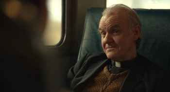 Movie still from “The Tender Bar” (2021), directed by George Clooney – An older man sitting in a chair on a train; Close Up shot, Over the shoulder angle