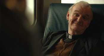 Movie still from “The Tender Bar” (2021), directed by George Clooney – An older man sitting in a chair smiling; Close Up shot, Over the shoulder angle