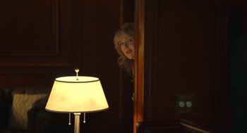 Movie still from “The Tender Bar” (2021), directed by George Clooney – A woman standing in front of a lamp in a room; Medium shot, Over the shoulder angle