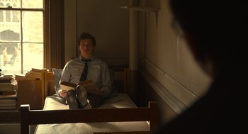 Movie still from “The Tender Bar” (2021), directed by George Clooney – A man sitting on top of a bed in a room; Medium shot, High angle