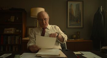 Movie still from “The Tender Bar” (2021), directed by George Clooney – An older man sitting at a desk looking at a piece of paper; Medium shot, Over the shoulder angle