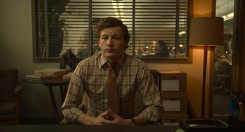 Movie still from “The Tender Bar” (2021), directed by George Clooney – A man sitting at a table wearing a plaid shirt; Medium shot, Over the shoulder angle