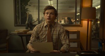 Movie still from “The Tender Bar” (2021), directed by George Clooney – A man sitting at a desk in front of papers; Medium shot, Low angle