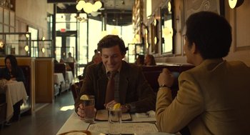 Movie still from “The Tender Bar” (2021), directed by George Clooney – A man sitting at a table with a glass of water; Medium shot, Over the shoulder angle