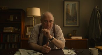 Movie still from “The Tender Bar” (2021), directed by George Clooney – An older man sitting at a desk in a room; Medium shot, Low angle