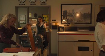 Movie still from “The Tender Bar” (2021), directed by George Clooney – A woman sitting in a chair holding a remote control; Medium shot, Over the shoulder angle