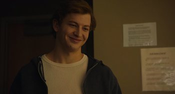 Movie still from “The Tender Bar” (2021), directed by George Clooney – A young man smiling for the camera in front of a wall; Close Up shot, Over the shoulder angle