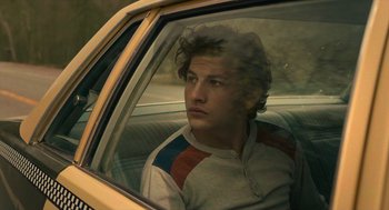 Movie still from “The Tender Bar” (2021), directed by George Clooney – A man sitting in the back seat of a car; Medium shot, Low angle