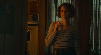 Movie still from “The Tender Bar” (2021), directed by George Clooney – A woman holding a glass of water while standing in a kitchen; Medium shot, Over the shoulder angle