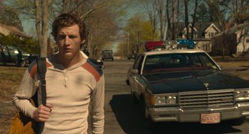 Movie still from “The Tender Bar” (2021), directed by George Clooney – A man standing on the side of the road in front of a cop car; Medium shot, Low angle