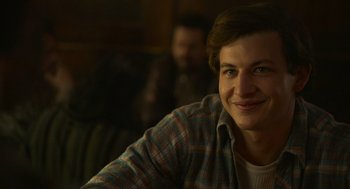 Movie still from “The Tender Bar” (2021), directed by George Clooney – A man sitting in front of a camera smiling; Close Up shot, Over the shoulder angle