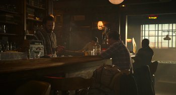 Movie still from “The Tender Bar” (2021), directed by George Clooney – Two men sitting at a table in front of a bar; Medium shot, Over the shoulder angle