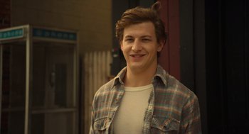 Movie still from “The Tender Bar” (2021), directed by George Clooney – A young man smiling for the camera in front of a building; Close Up shot, Over the shoulder angle