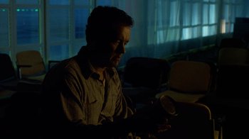 Movie still from “The Terminal” (2004), directed by Steven Spielberg – A man sitting at a table looking at his cell phone; Medium shot, Low angle
