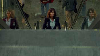 Movie still from “The Terminal” (2004), directed by Steven Spielberg – A woman in a business suit riding an escalator; Medium shot, Over the shoulder angle