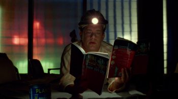 Movie still from “The Terminal” (2004), directed by Steven Spielberg – A man reading a new york city book with a headlamp on; Medium shot, High angle