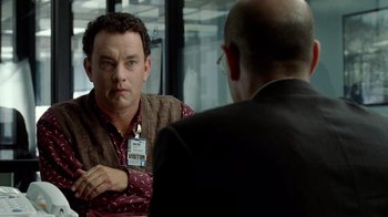 Movie still from “The Terminal” (2004), directed by Steven Spielberg – A man wearing a name tag talking to another man in front of a window; Medium shot, Over the shoulder angle