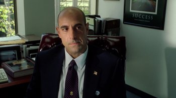 Movie still from “The Terminal” (2004), directed by Steven Spielberg – A man in a suit and tie sitting in a chair; Close Up shot, High angle