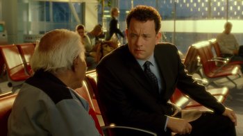 Movie still from “The Terminal” (2004), directed by Steven Spielberg – A man in a suit and tie talking to another man in a suit and tie; Medium shot, Over the shoulder angle