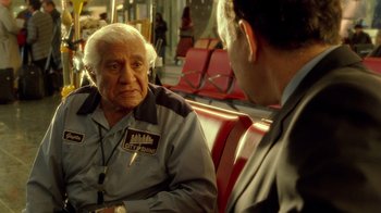 Movie still from “The Terminal” (2004), directed by Steven Spielberg – An older man sitting next to another man on a bus; Medium shot, Over the shoulder angle