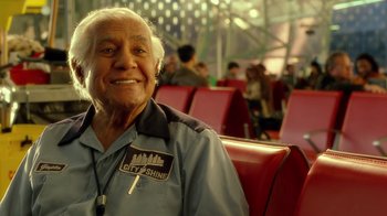 Movie still from “The Terminal” (2004), directed by Steven Spielberg – An older man sitting on a red chair in an airport; Close Up shot, Over the shoulder angle