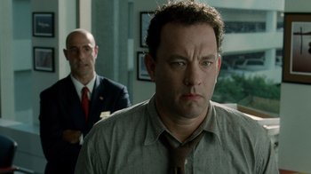 Movie still from “The Terminal” (2004), directed by Steven Spielberg – A man in a suit and tie standing next to another man in a suit and tie; Close Up shot, Over the shoulder angle