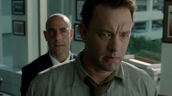 Movie still from “The Terminal” (2004), directed by Steven Spielberg – A man standing next to another man in front of a window; Close Up shot, Over the shoulder angle