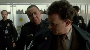 Movie still from “The Terminal” (2004), directed by Steven Spielberg – A man in a suit and tie standing next to another man in a uniform; Close Up shot, Over the shoulder angle