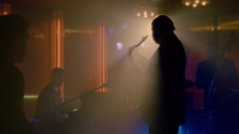 Movie still from “The Terminal” (2004), directed by Steven Spielberg – A man playing a saxophone in a dark room; Wide shot, Over the shoulder angle