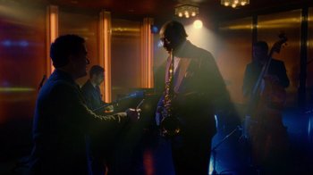 Movie still from “The Terminal” (2004), directed by Steven Spielberg – A man playing a saxophone in front of other men; Wide shot, Low angle