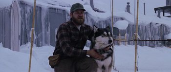Movie still from “The Thing” (1982), directed by John Carpenter – A man kneeling down next to a husky dog; Medium shot, Low angle