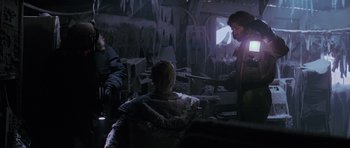 Movie still from “The Thing” (1982), directed by John Carpenter – A group of people standing around in a room; Medium shot, Over the shoulder angle