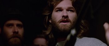Movie still from “The Thing” (1982), directed by John Carpenter – A man with long hair and a goatee looking upward; Close Up shot, Low angle