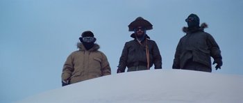 Movie still from “The Thing” (1982), directed by John Carpenter – A group of men standing on top of a snow covered slope; Medium shot, Low angle
