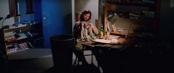 Movie still from “The Thing” (1982), directed by John Carpenter – A man sitting at a table in front of a trashcan; Medium shot, High angle