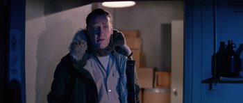 Movie still from “The Thing” (1982), directed by John Carpenter – A man in a parka and scarf standing in a dimly - lit room; Medium shot, Over the shoulder angle