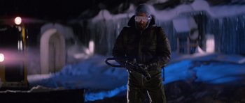 Movie still from “The Thing” (1982), directed by John Carpenter – A man holding a saw in front of a waterfall; Medium shot, Low angle