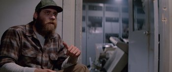 Movie still from “The Thing” (1982), directed by John Carpenter – A man with a beard wearing a hat sitting in a room; Close Up shot, Low angle