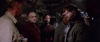 Movie still from “The Thing” (1982), directed by John Carpenter – A group of men standing next to each other in a room; Medium shot, Over the shoulder angle