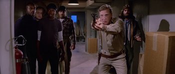 Movie still from “The Thing” (1982), directed by John Carpenter – A group of men standing in a room holding guns; Medium shot, Low angle