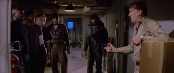 Movie still from “The Thing” (1982), directed by John Carpenter – A man taking a picture of two men with a gun; Medium shot, Over the shoulder angle