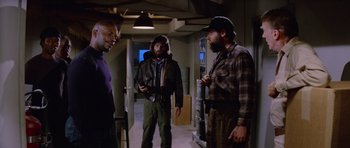 Movie still from “The Thing” (1982), directed by John Carpenter – A group of men standing next to each other in a room; Medium shot, Low angle