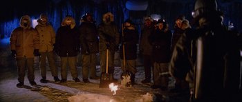 Movie still from “The Thing” (1982), directed by John Carpenter – A group of people standing around a fire; Wide shot, High angle