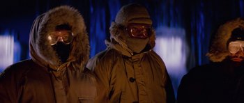 Movie still from “The Thing” (1982), directed by John Carpenter – A man in a parka is standing next to another man in a parka; Medium shot, Low angle