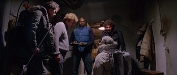 Movie still from “The Thing” (1982), directed by John Carpenter – A group of people standing around a white dog; Medium shot, Over the shoulder angle