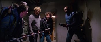 Movie still from “The Thing” (1982), directed by John Carpenter – A group of men standing next to each other in a room; Medium shot, Low angle