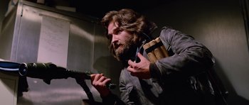 Movie still from “The Thing” (1982), directed by John Carpenter – A man with long hair and a beard holding a gun; Medium shot, Low angle